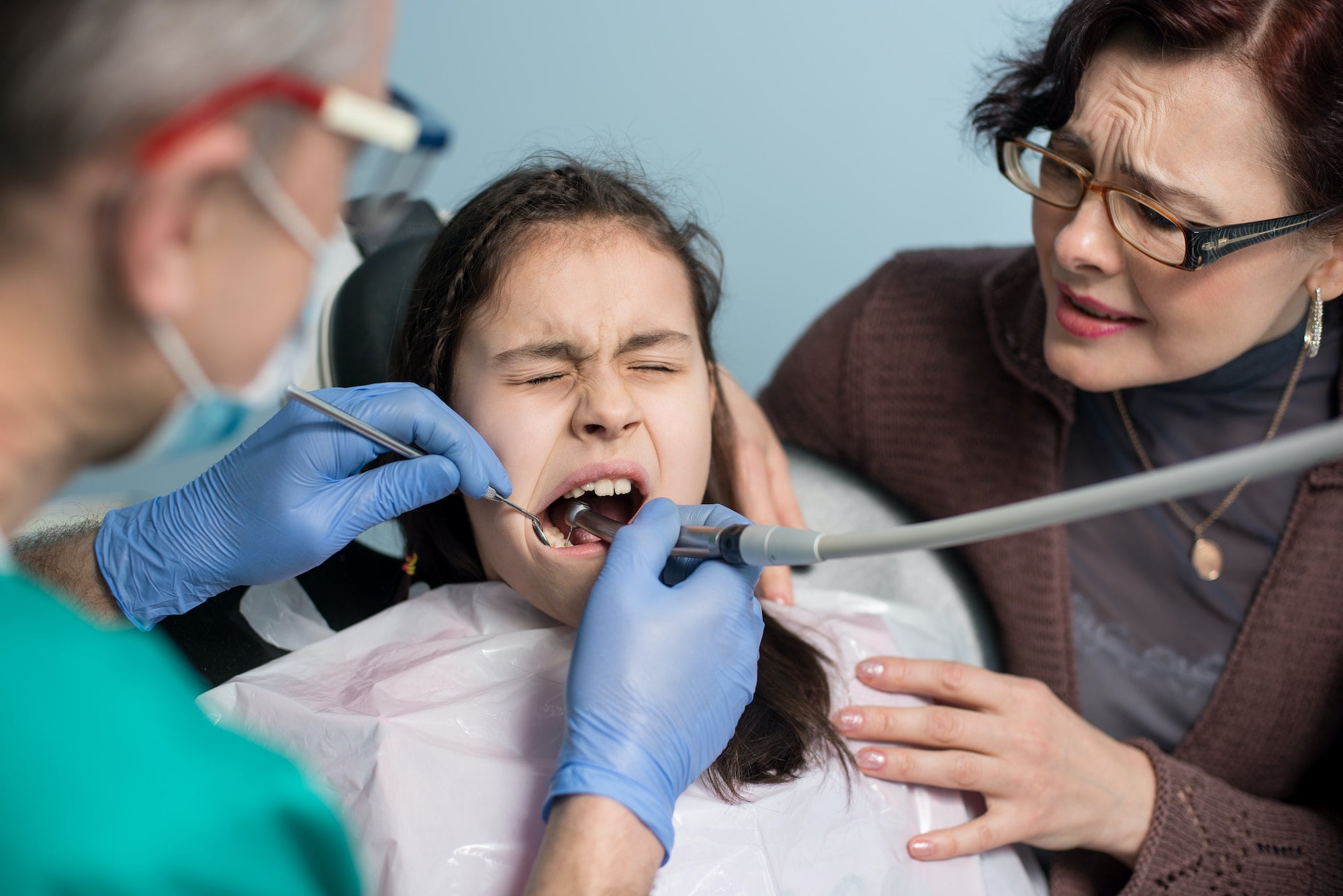 Girl with on the first dental visit. Senior pediatric dentist with mother treating patient teeth